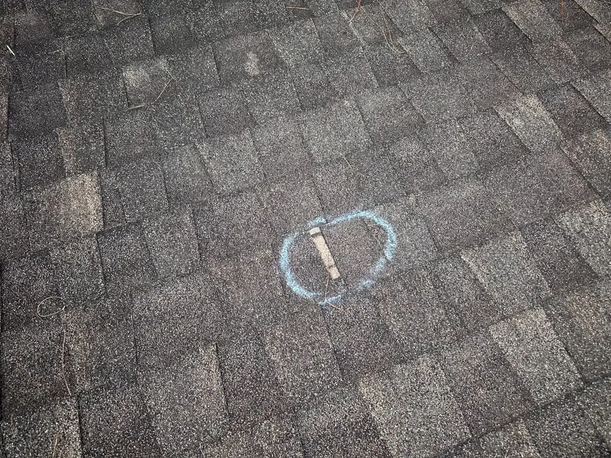 Hail strike circled in chalk on an asphalt shingle during a Metro Builders inspection